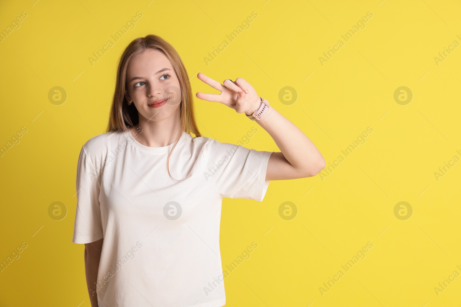 Photo of Teenage girl showing v-sign on yellow background