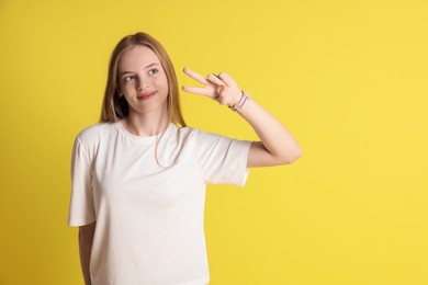 Teenage girl showing v-sign on yellow background