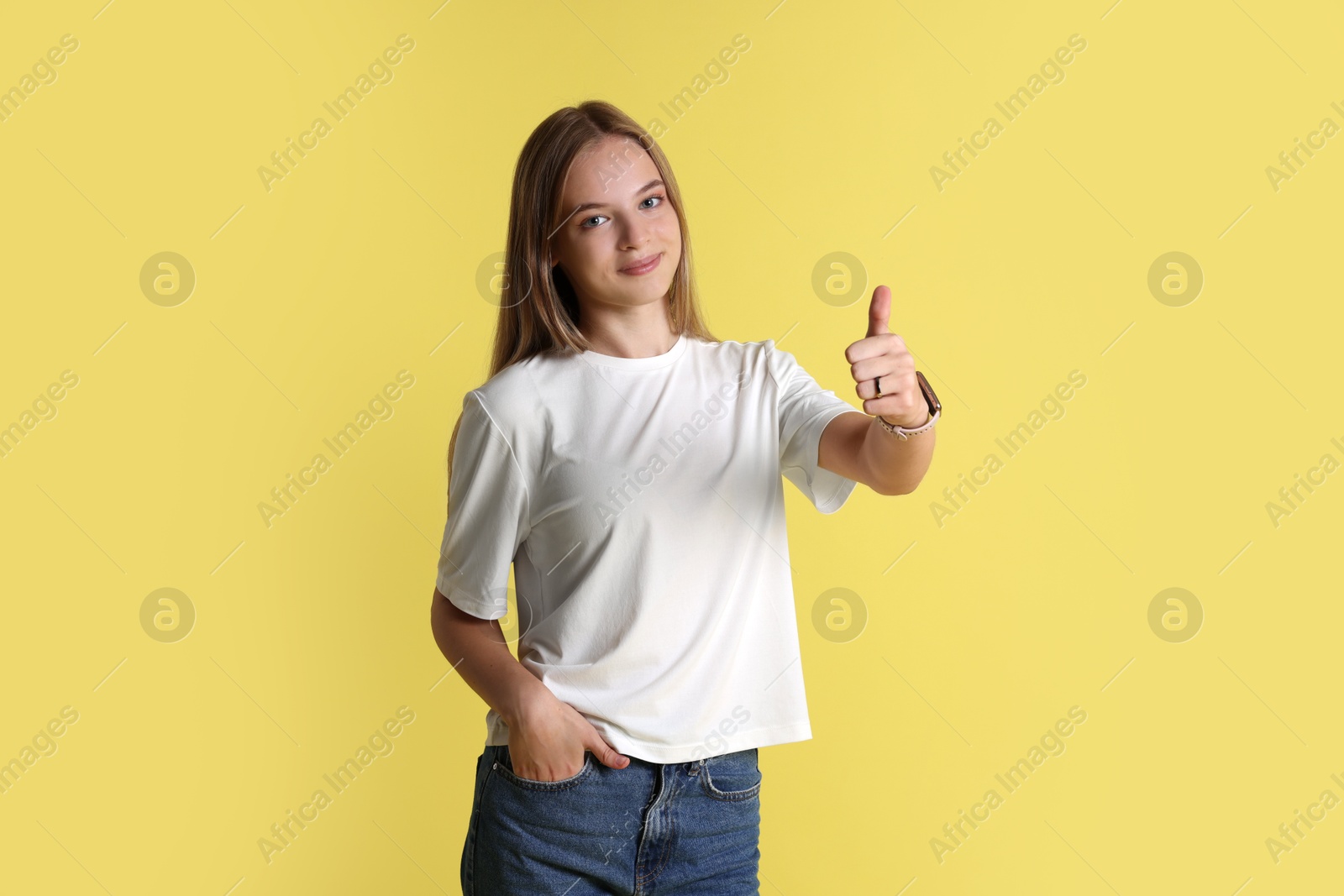 Photo of Teenage girl showing thumbs up on yellow background