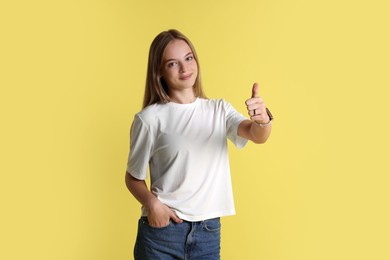 Teenage girl showing thumbs up on yellow background