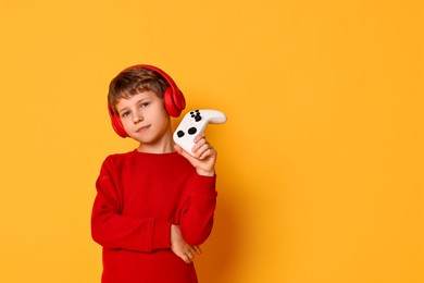 Photo of Cute little boy in headphones with controller on orange background. Space for text