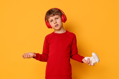 Cute little boy in headphones with controller on orange background