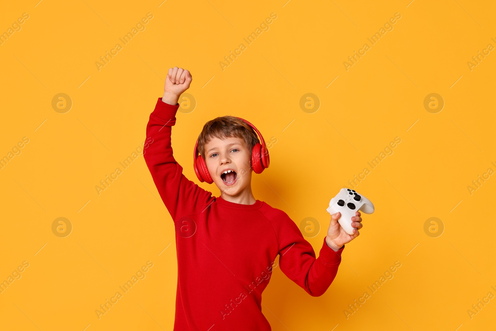 Photo of Happy little boy in headphones with controller on orange background