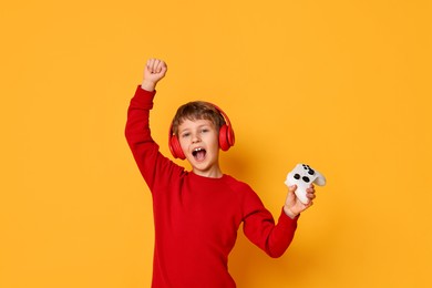 Photo of Happy little boy in headphones with controller on orange background