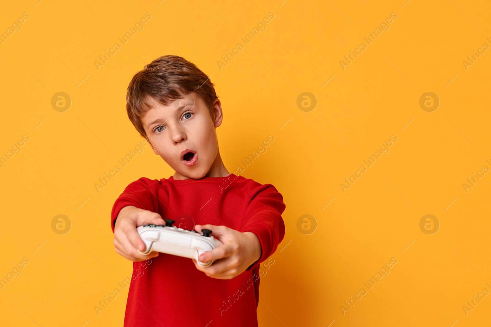 Photo of Cute little boy playing video game with controller on orange background. Space for text