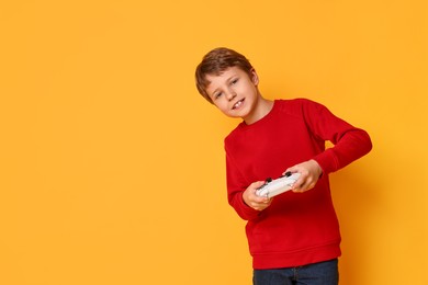 Happy little boy playing video game with controller on orange background. Space for text