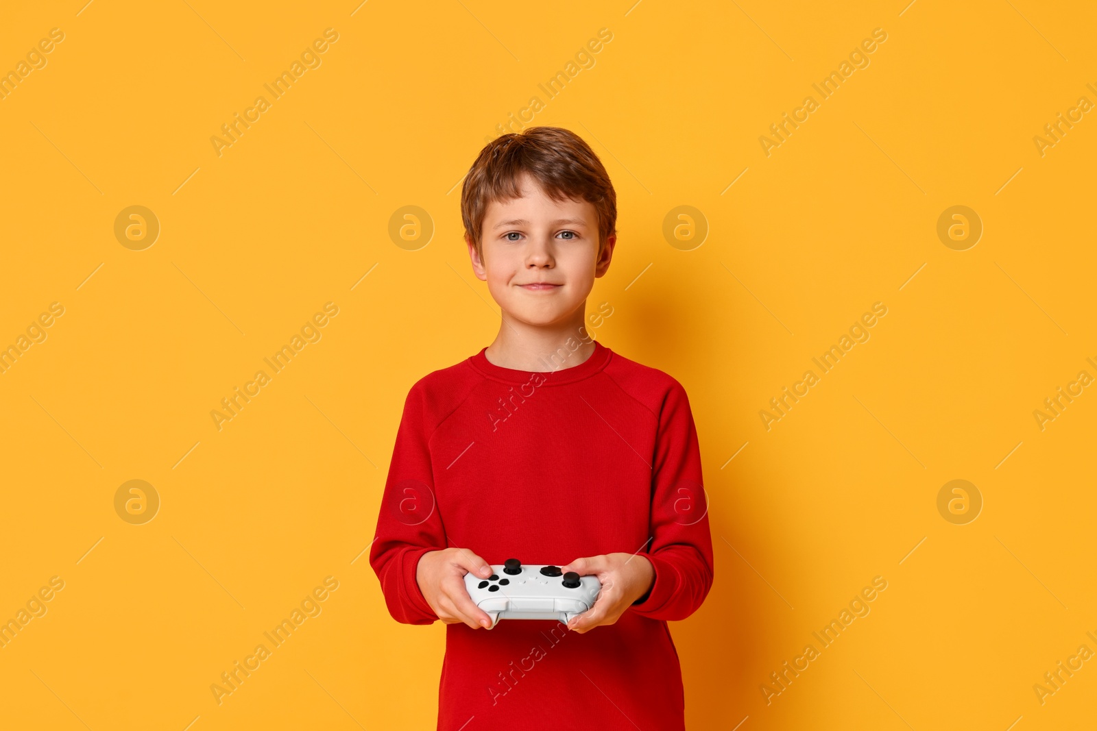 Photo of Happy little boy playing video game with controller on orange background