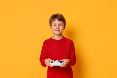 Happy little boy playing video game with controller on orange background