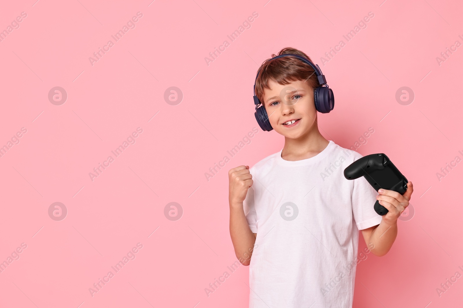 Photo of Happy little boy in headphones with controller on pink background. Space for text