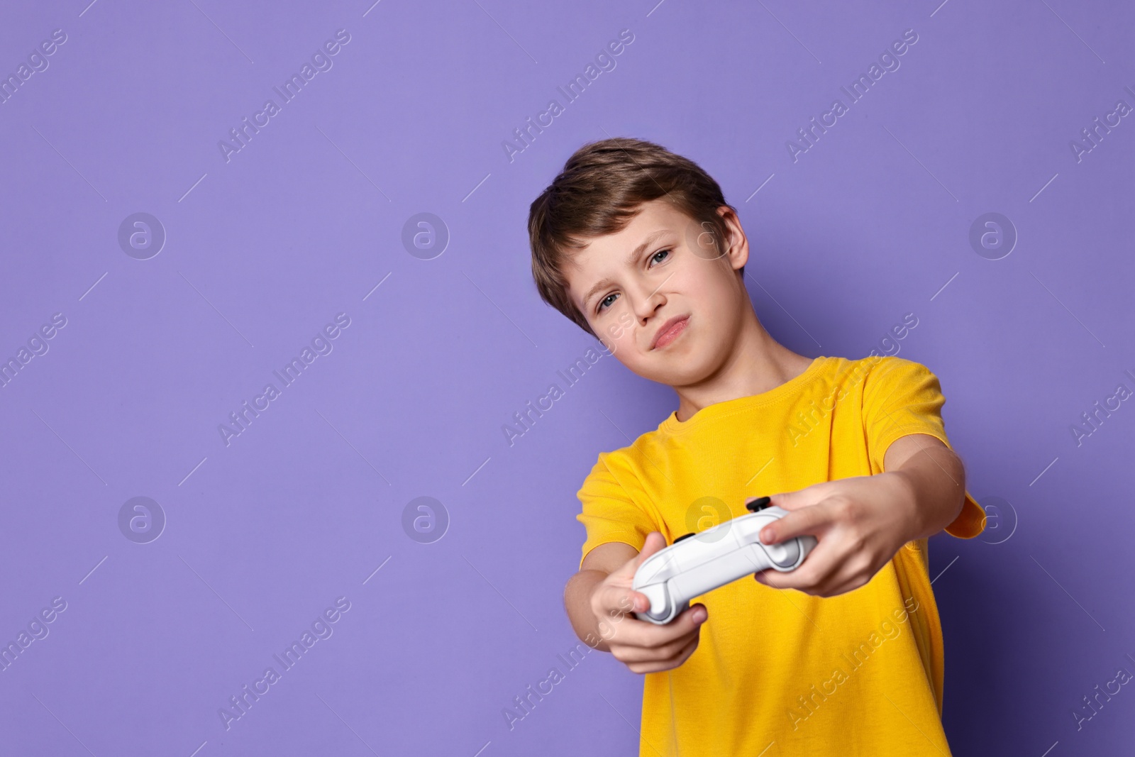 Photo of Cute little boy playing video game with controller on purple background. Space for text