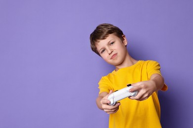 Cute little boy playing video game with controller on purple background. Space for text