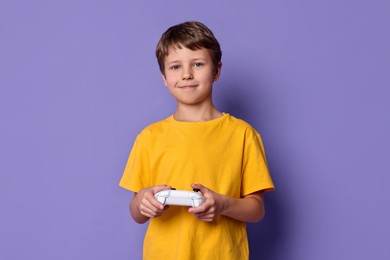 Cute little boy playing video game with controller on purple background