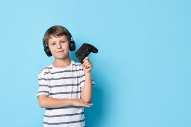 Photo of Cute little boy in headphones with controller on light blue background. Space for text