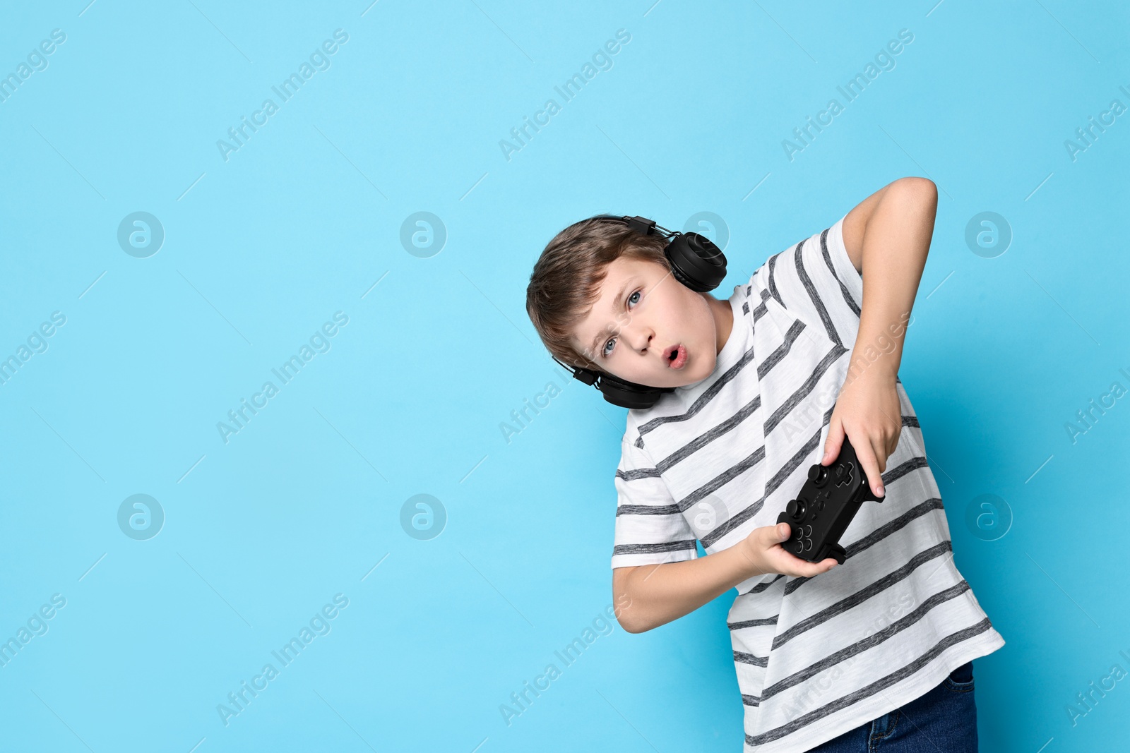 Photo of Cute little boy in headphones playing video game with controller on light blue background. Space for text