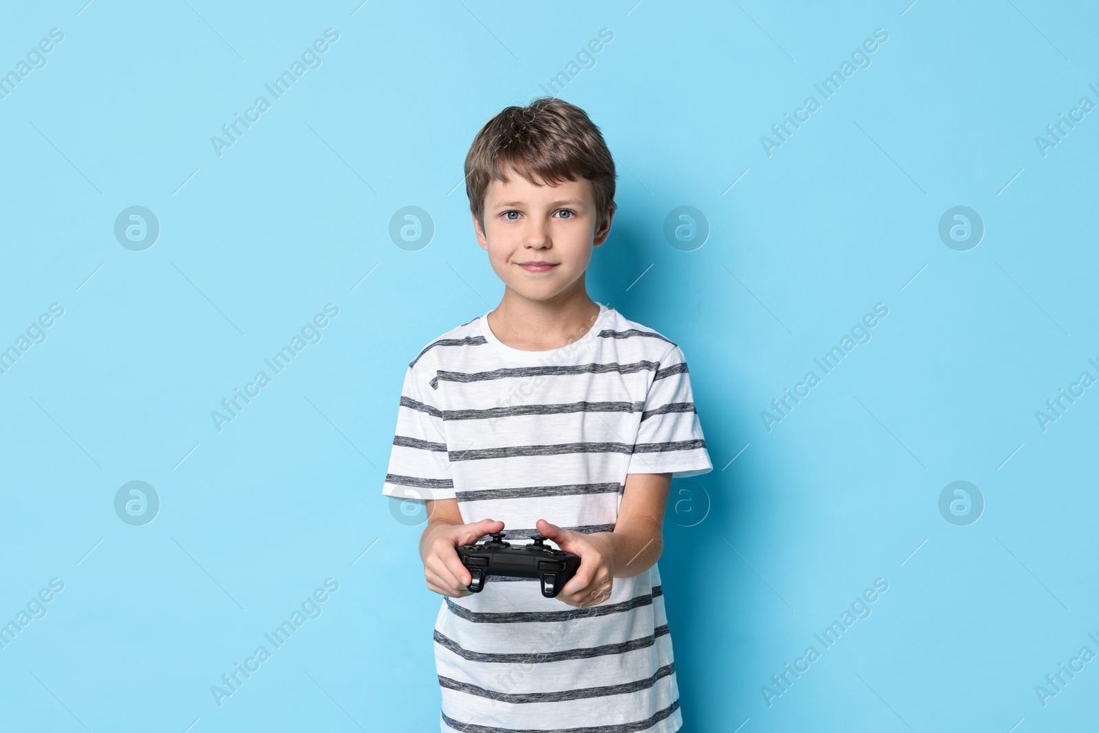 Photo of Cute little boy playing video game with controller on light blue background