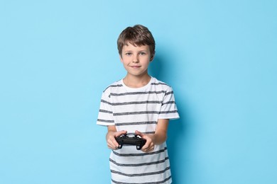 Cute little boy playing video game with controller on light blue background