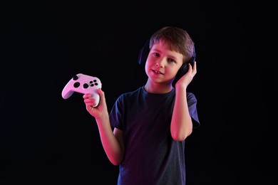 Photo of Happy little boy in headphones with controller on black background