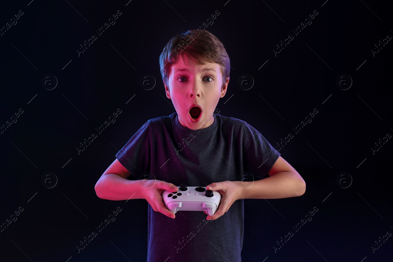 Photo of Cute little boy playing video game with controller on black background