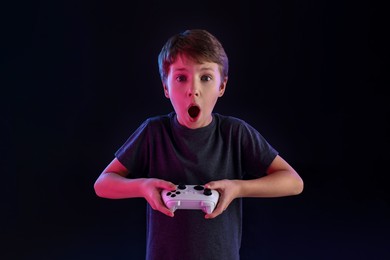 Cute little boy playing video game with controller on black background