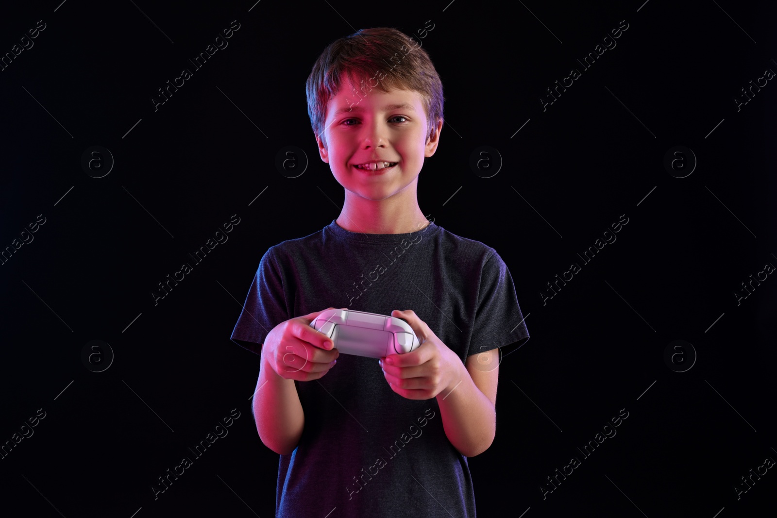 Photo of Happy little boy playing video game with controller on black background