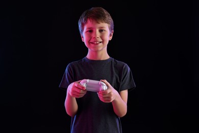 Happy little boy playing video game with controller on black background