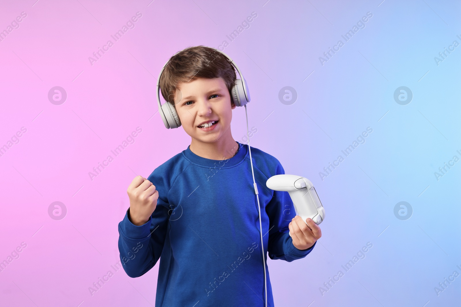 Photo of Happy little boy in headphones with controller on color background