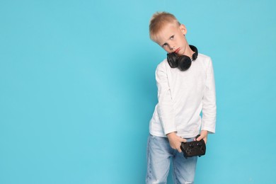 Cute little boy with headphones and controller on light blue background. Space for text