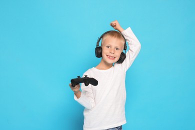 Happy little boy in headphones with controller on light blue background