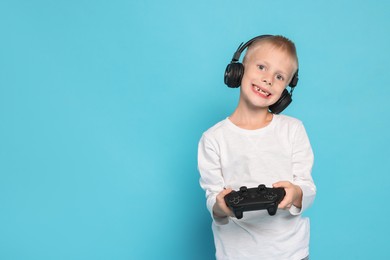 Photo of Happy little boy in headphones playing video game with controller on light blue background. Space for text