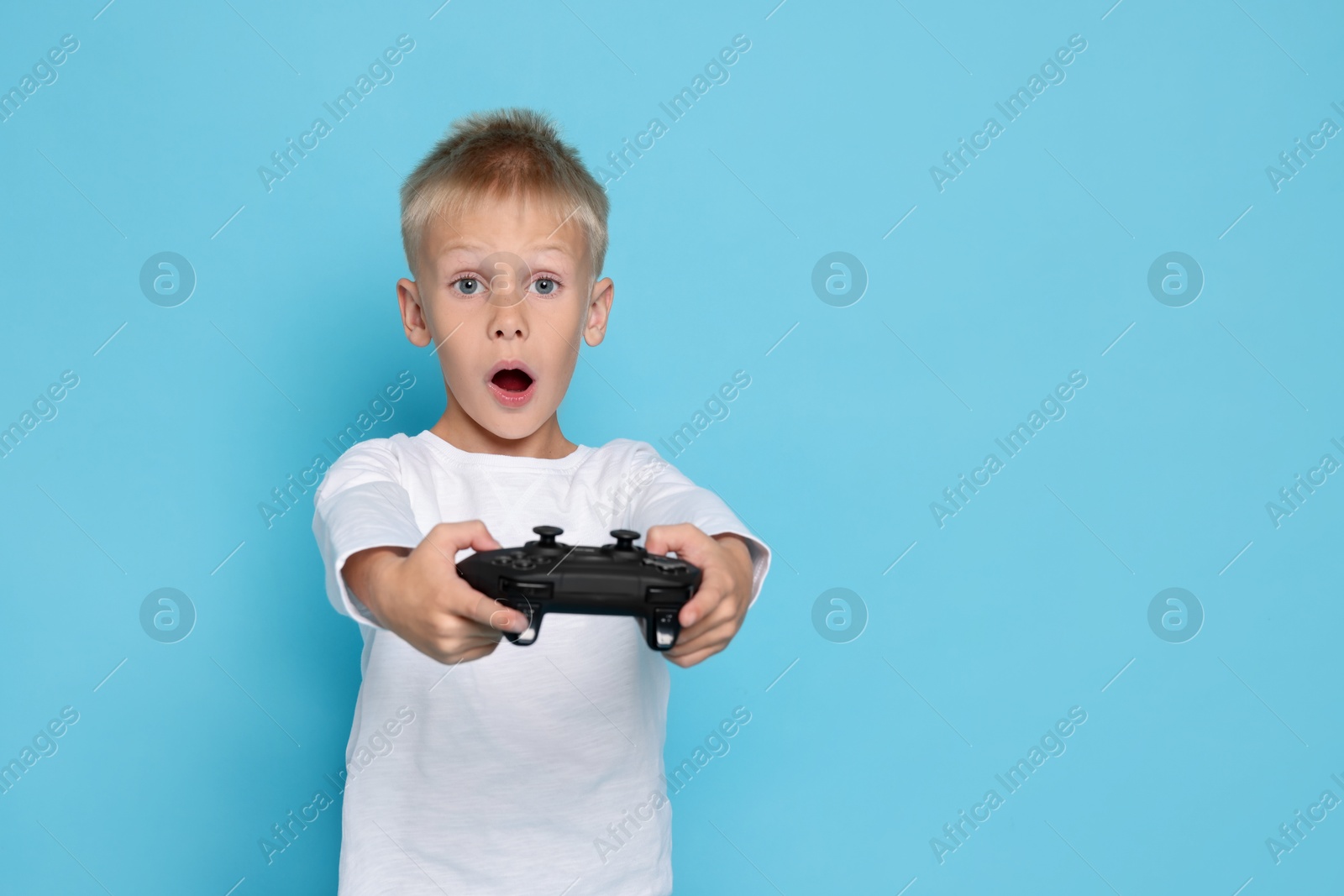 Photo of Cute little boy playing video game with controller on light blue background. Space for text