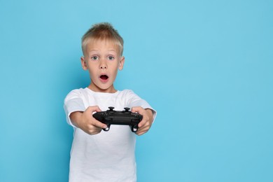 Cute little boy playing video game with controller on light blue background. Space for text