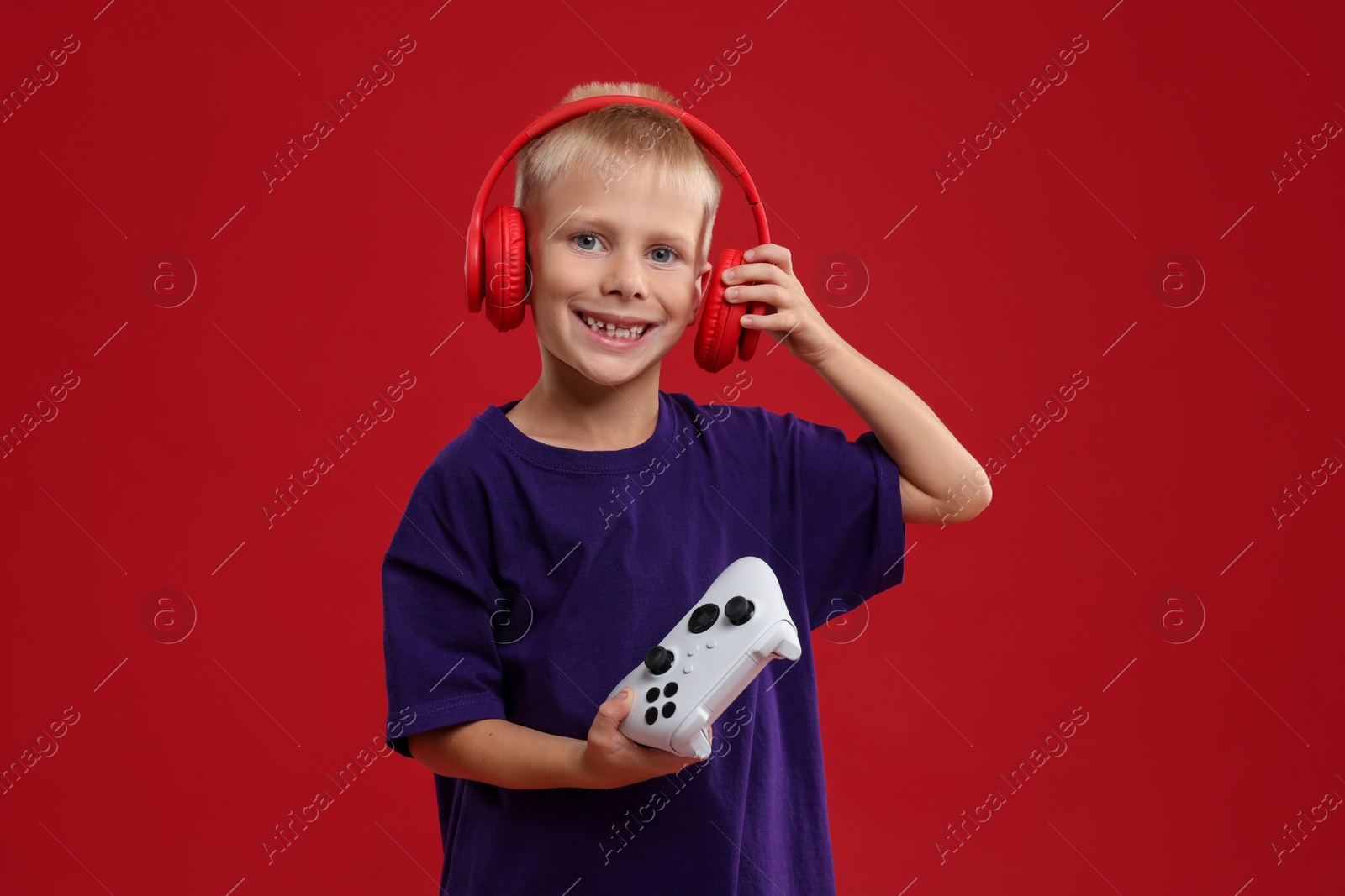 Photo of Happy little boy with headphones and controller on red background