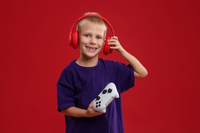 Happy little boy with headphones and controller on red background