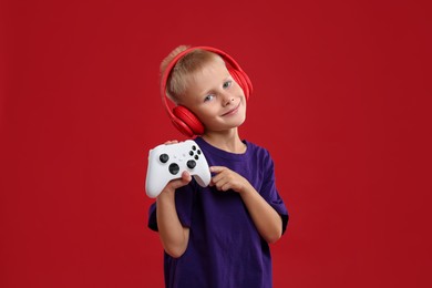 Photo of Cute little boy in headphones pointing at controller on red background