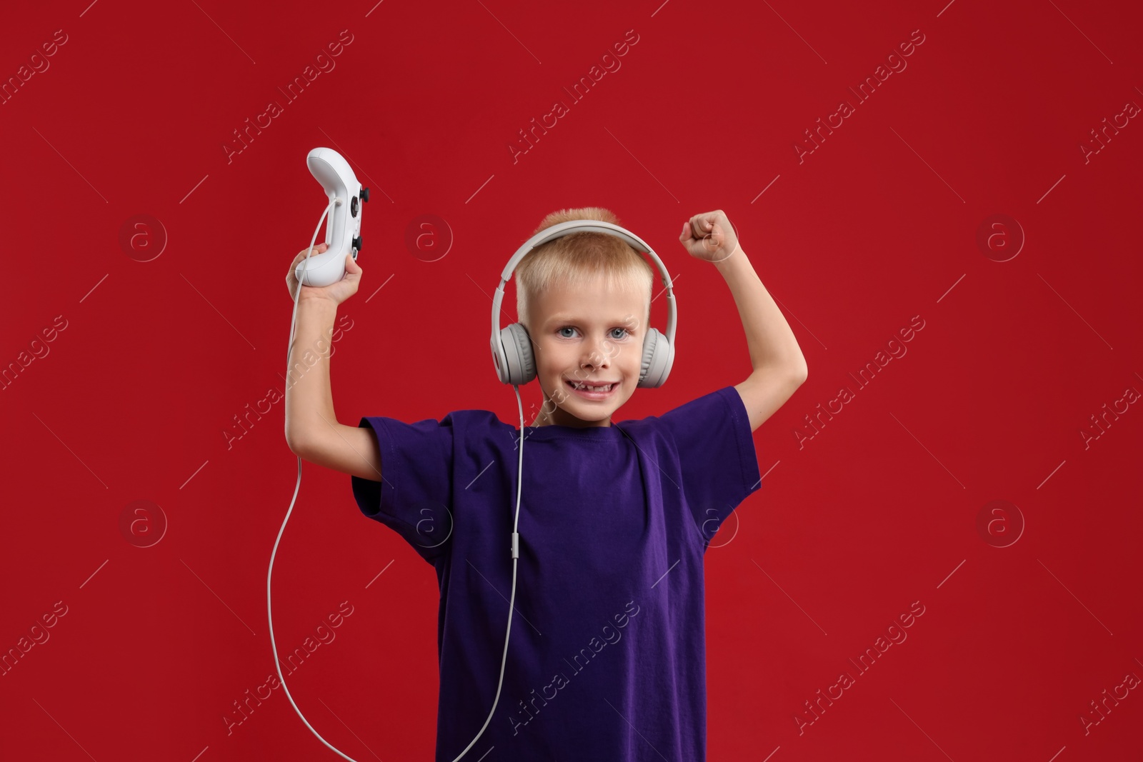 Photo of Cute little boy in headphones with controller on red background