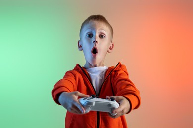 Cute little boy playing video game with controller on color background