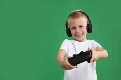 Happy little boy in headphones playing video game with controller on green background. Space for text