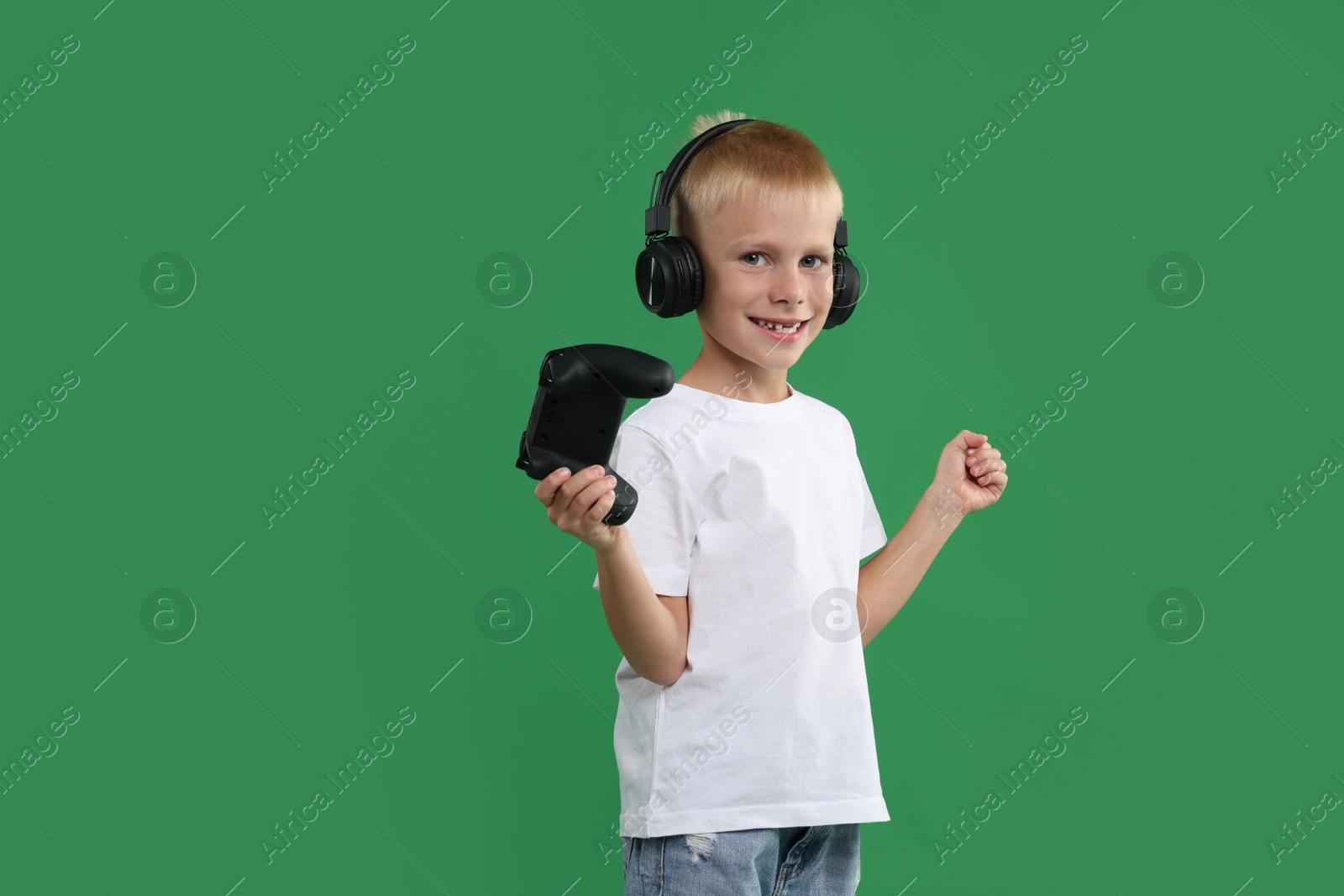 Photo of Happy little boy in headphones with controller on green background. Space for text