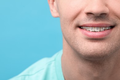 Smiling man with dental braces on light blue background, closeup. Space for text