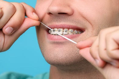 Photo of Man with braces cleaning teeth using dental floss on light blue background, closeup