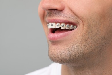 Happy man with dental braces on grey background, closeup. Space for text