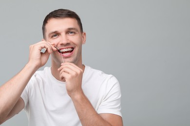 Happy man with braces cleaning teeth using dental floss on grey background. Space for text