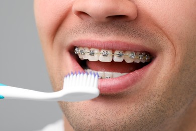 Man with dental braces cleaning teeth on grey background, closeup