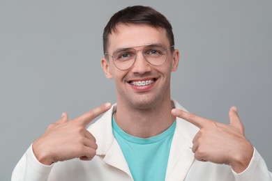 Happy man pointing at his dental braces on grey background