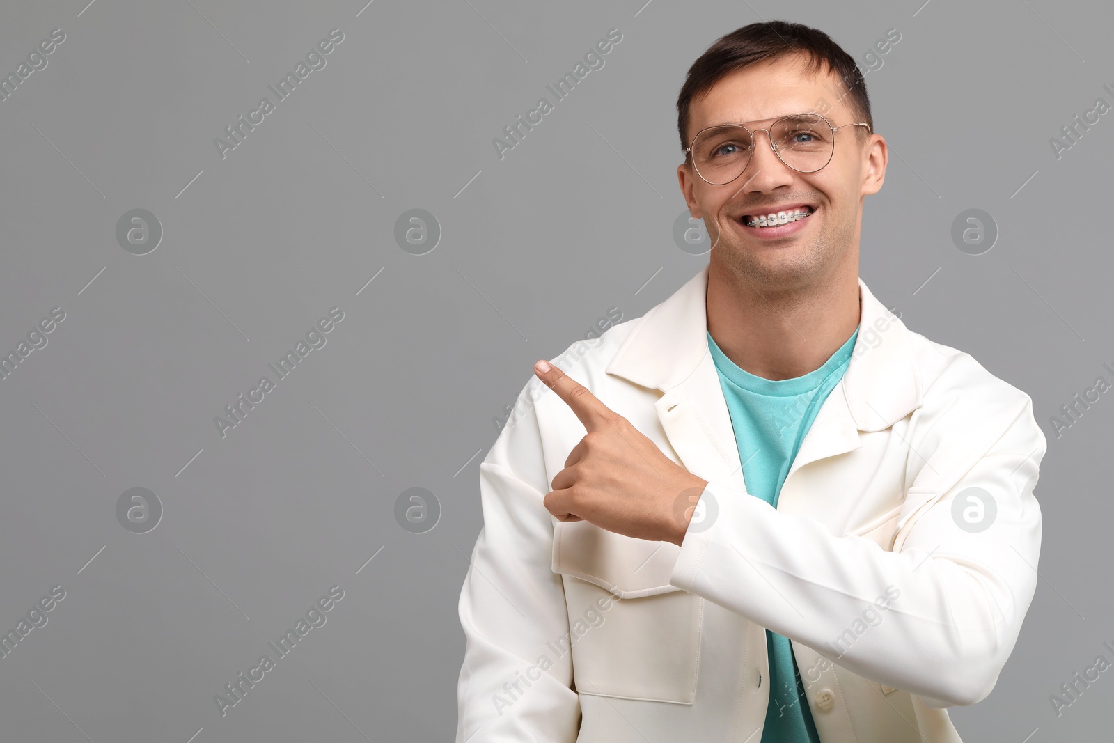 Photo of Smiling man with dental braces pointing at something on grey background. Space for text