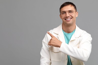 Smiling man with dental braces pointing at something on grey background. Space for text