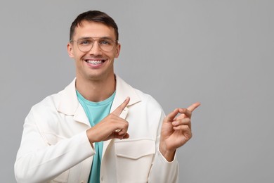 Smiling man with dental braces pointing at something on grey background. Space for text