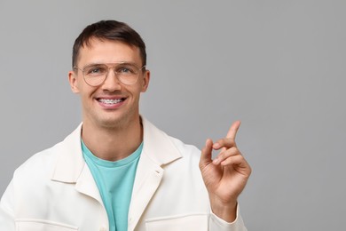 Photo of Smiling man with dental braces pointing at something on grey background. Space for text