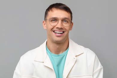 Smiling man with dental braces on grey background