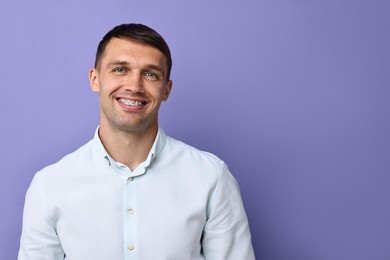 Smiling man with dental braces on violet background. Space for text